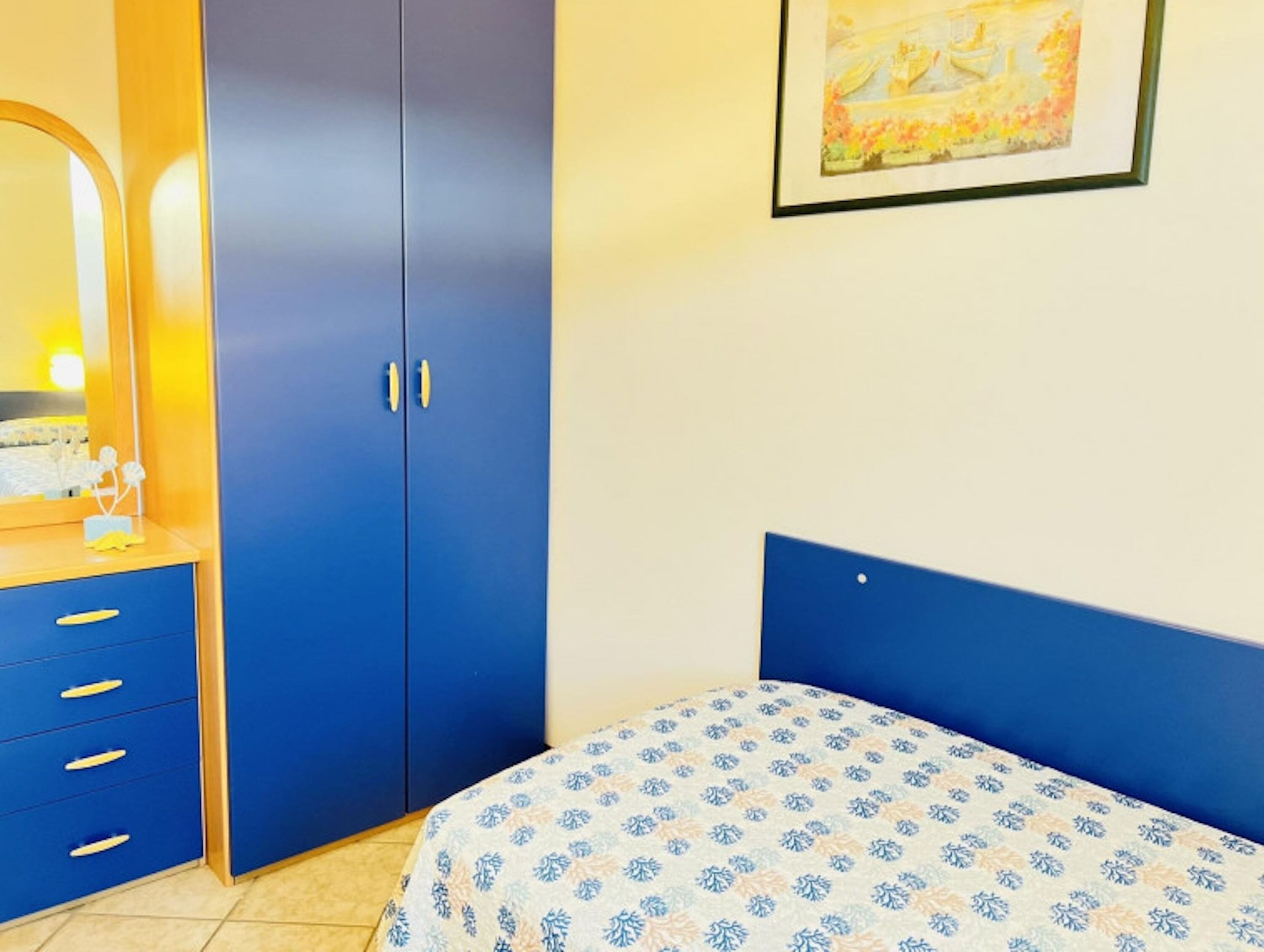 A bedroom with a bed, a wardrobe, a dresser, and a framed picture on the wall.