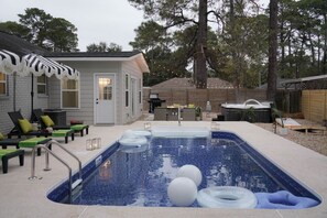 Piscina com espreguiçadeiras e banheira de hidromassagem em um quintal.