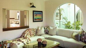 Een woonkamer met een bank, een bijzettafeltje, een ingelijst kunstwerk en een rond raam.
