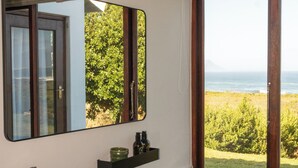 Een badkamer met een zwart wastafel, een spiegel, een raam met uitzicht op de oceaan en een betegelde vloer.