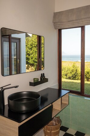 A bathroom with a black sink, a mirror, a window with a view of the ocean, and a tiled floor.