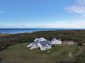 A modern white house with a sloped roof, surrounded by a well-maintained lawn and a view of the ocean.