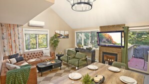 A spacious living room with a fireplace, a dining area with a wooden table set for four, and a comfortable seating area with a sofa and armchairs. - Cranmore home in North Conway|sleeps8|pet+ (Conway)