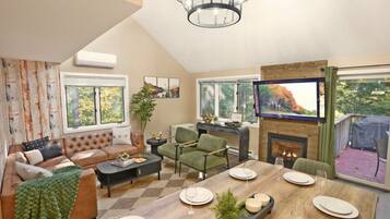 A spacious living room with a fireplace, a dining area with a wooden table set for four, and a comfortable seating area with a sofa and armchairs.
