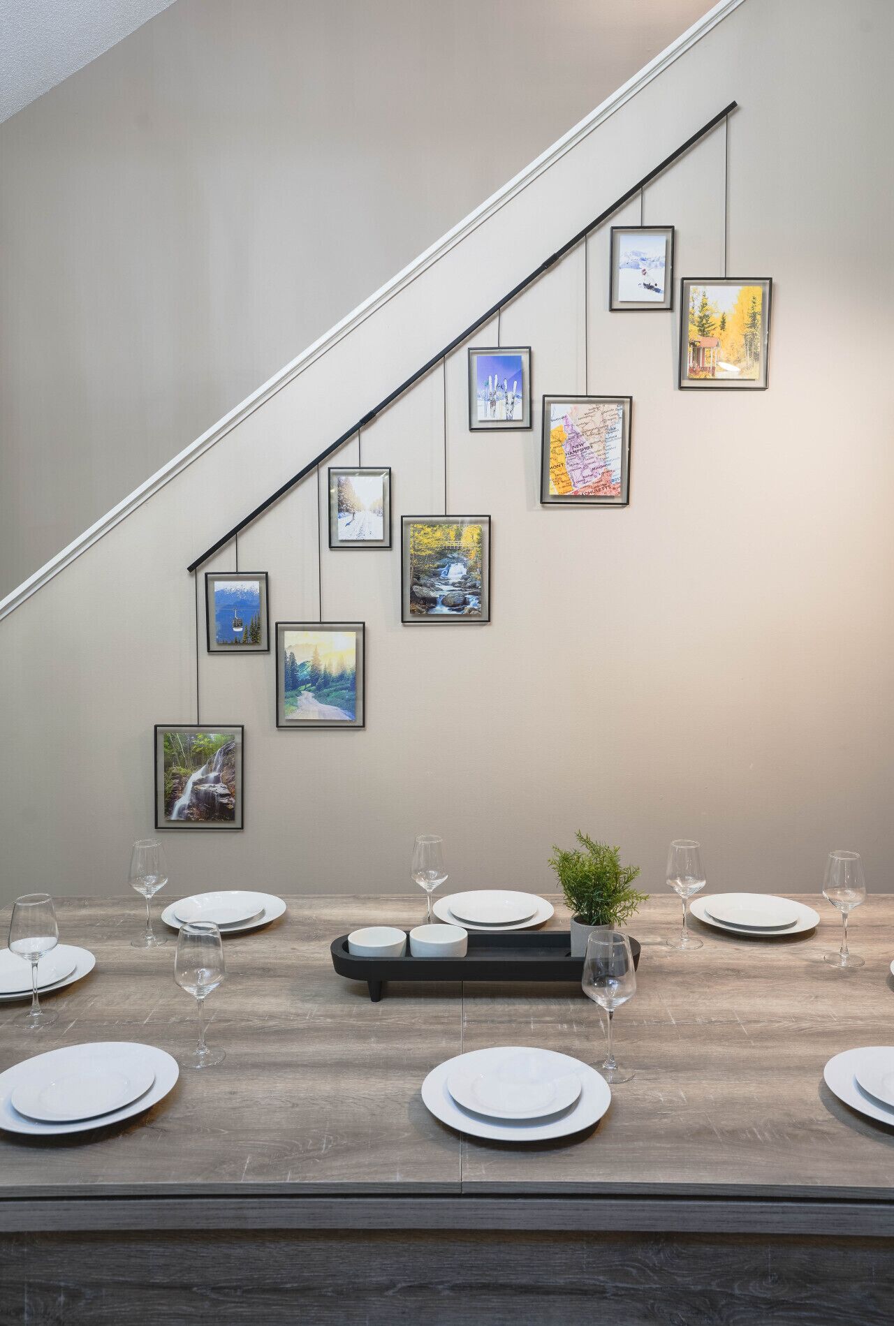 A dining area with a wooden table set for six, framed artwork on the wall, and a staircase.