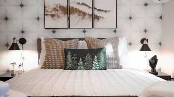 A neatly arranged bedroom with a bed, pillows, a nightstand, a lamp, and wall art.