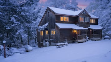 A wooden cabin with a porch and multiple windows, surrounded by snow-covered trees.