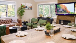 A dining area with a wooden table set for a meal, surrounded by green chairs and a sofa. - Cranmore home in North Conway|sleeps8|pet+ (Conway)