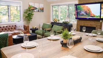 A dining area with a wooden table set for a meal, surrounded by green chairs and a sofa.