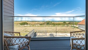 A balcony with wicker chairs, a view of the beach, and a clear sky.