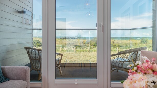 A balcony with wicker chairs, a cushioned bench, and a view of the beach.