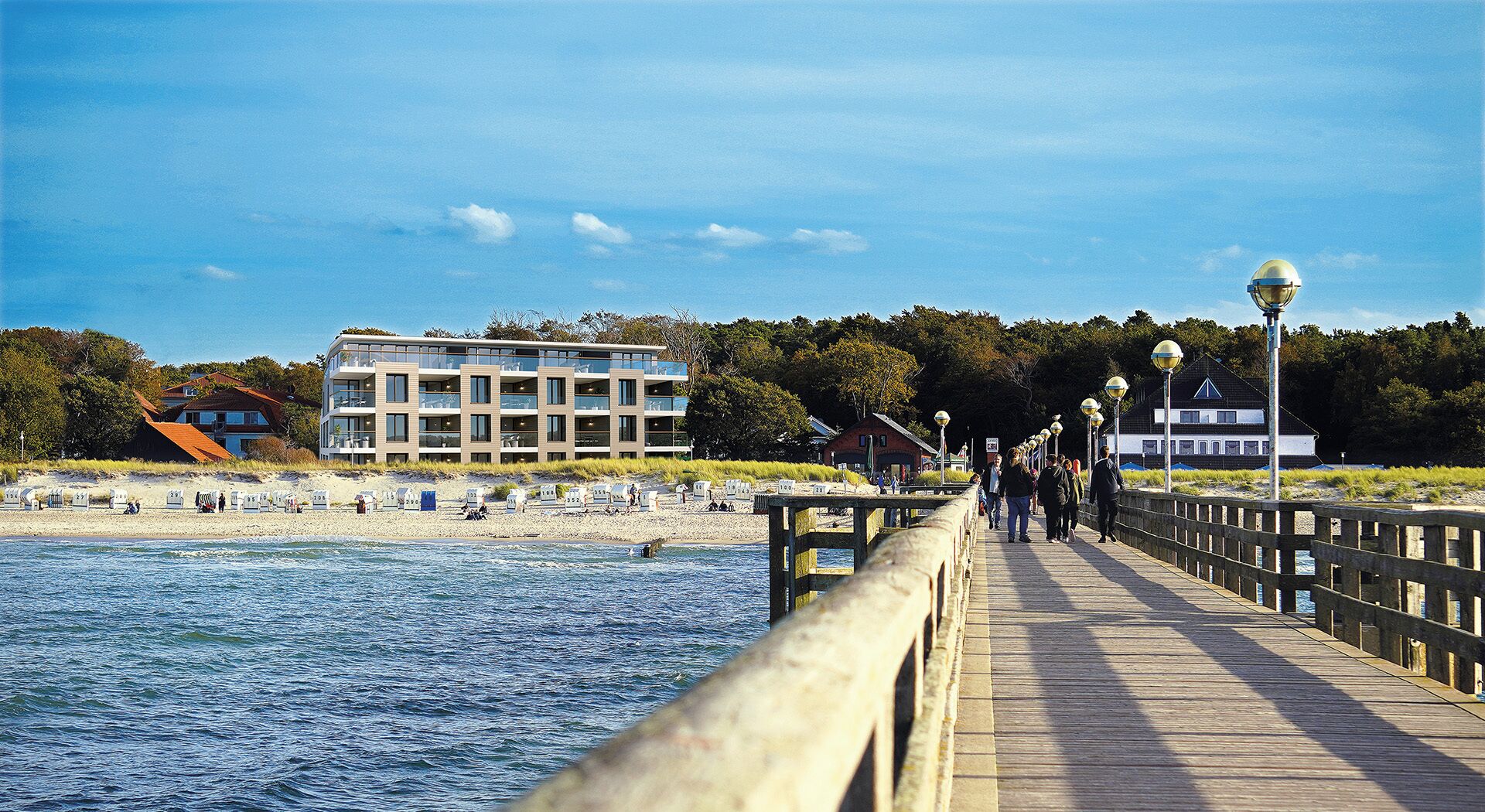 A wooden boardwalk leading to a beach with a modern building and a house in the background.