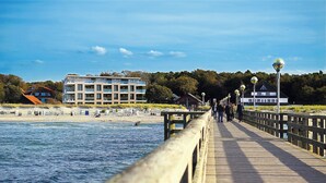 A wooden boardwalk leading to a beach with a modern building and a house in the background.