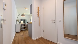 A hallway with wooden flooring, white walls, a coat rack, a door, and a mirror.