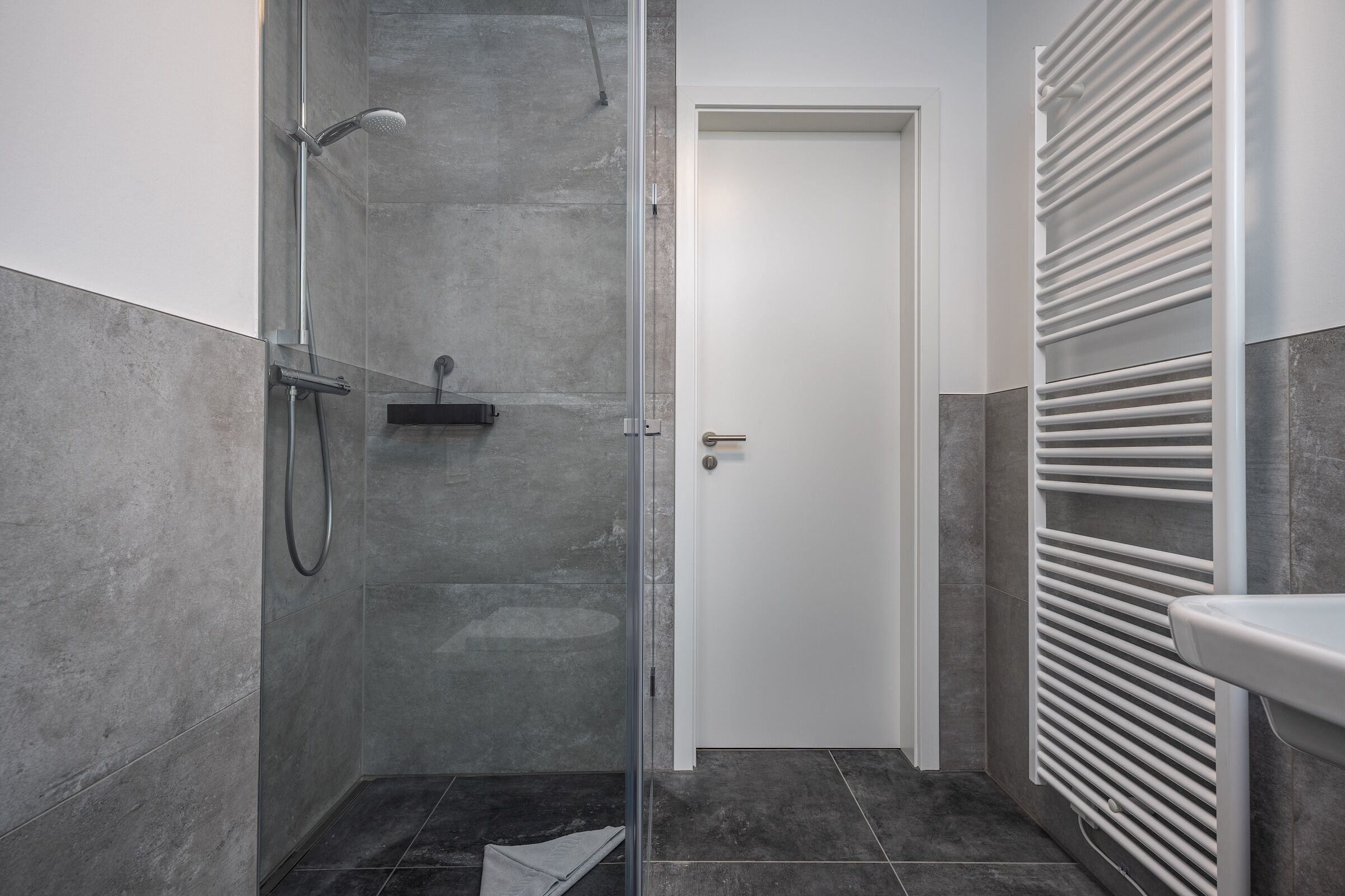 Une salle de bain moderne avec une cabine de douche en verre, une porte blanche et un radiateur encastré.