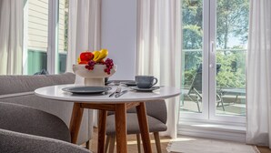 A dining area with a round table, grey sofa, and a window with curtains.