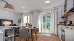 A modern kitchen with a dining area, wooden flooring, and a large window with curtains.