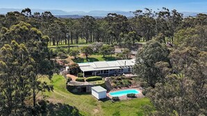 A modern house with a swimming pool, surrounded by a well-maintained lawn and dense trees.