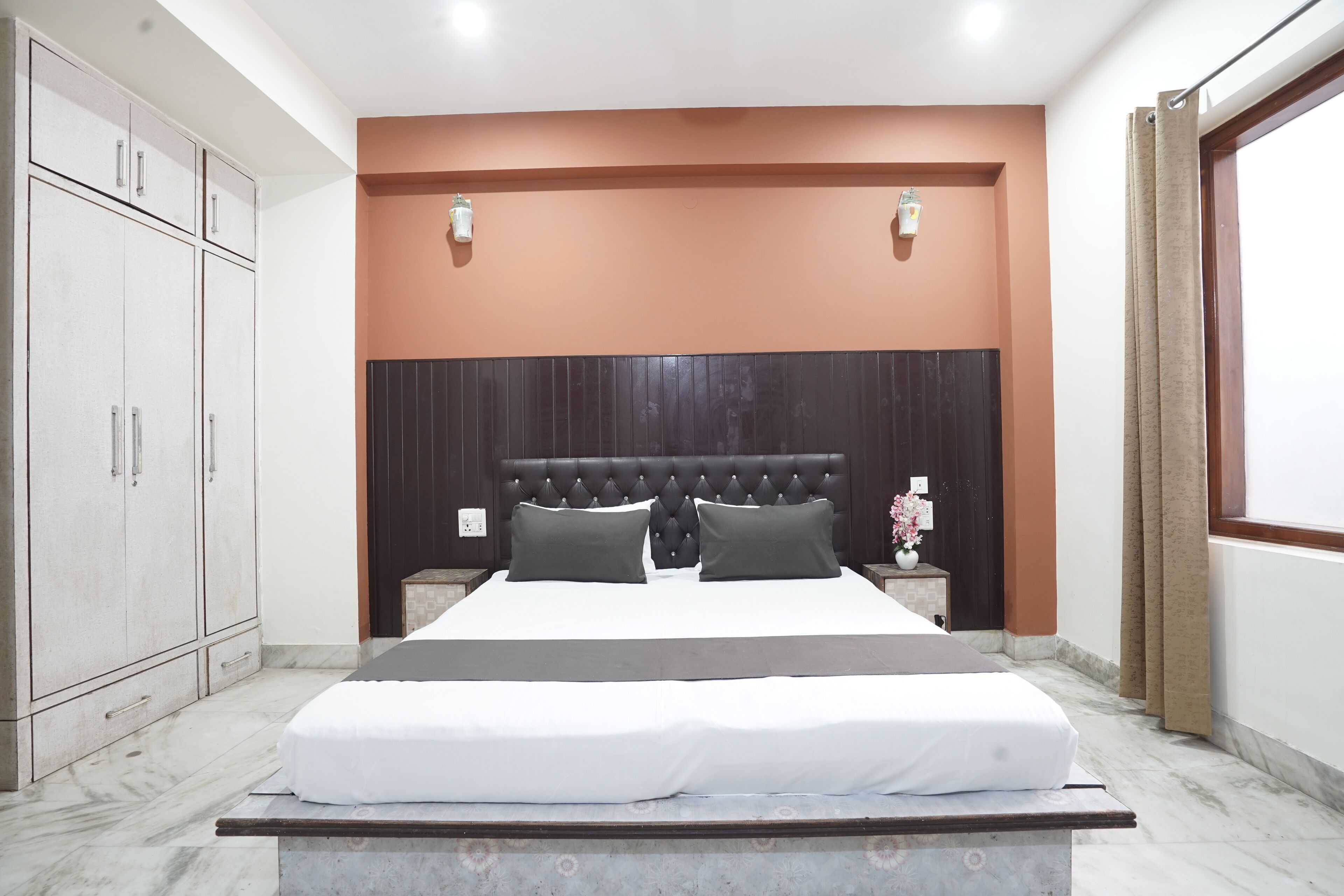 A neatly arranged bedroom with a large bed, a wardrobe, and a nightstand with a vase.