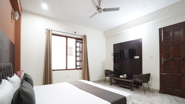 A hotel room with a bed, a desk, a chair, a TV, and a wardrobe. - Hotel Raj Mahal (Gurugram)