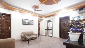 A room with a sofa, a coffee table, a ceiling fan, and a potted plant. - Hotel Raj Mahal (Gurugram)