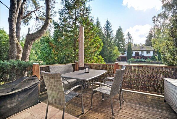 A deck with a table and chairs, surrounded by trees and a house in the background.