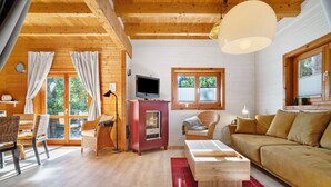 Een gezellig chaletinterieur met houten plafond, een bank, een televisie en een eethoek.