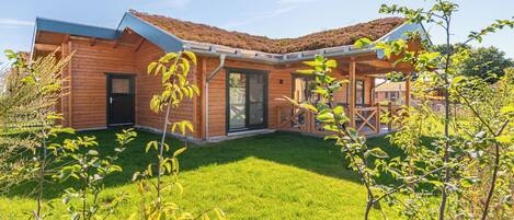 A modern wooden house with a sloped roof, a glass door entrance, and a well-maintained lawn.
