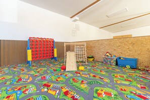 Une salle de jeux avec un tapis de jeu coloré, un filet d’escalade et divers jouets.