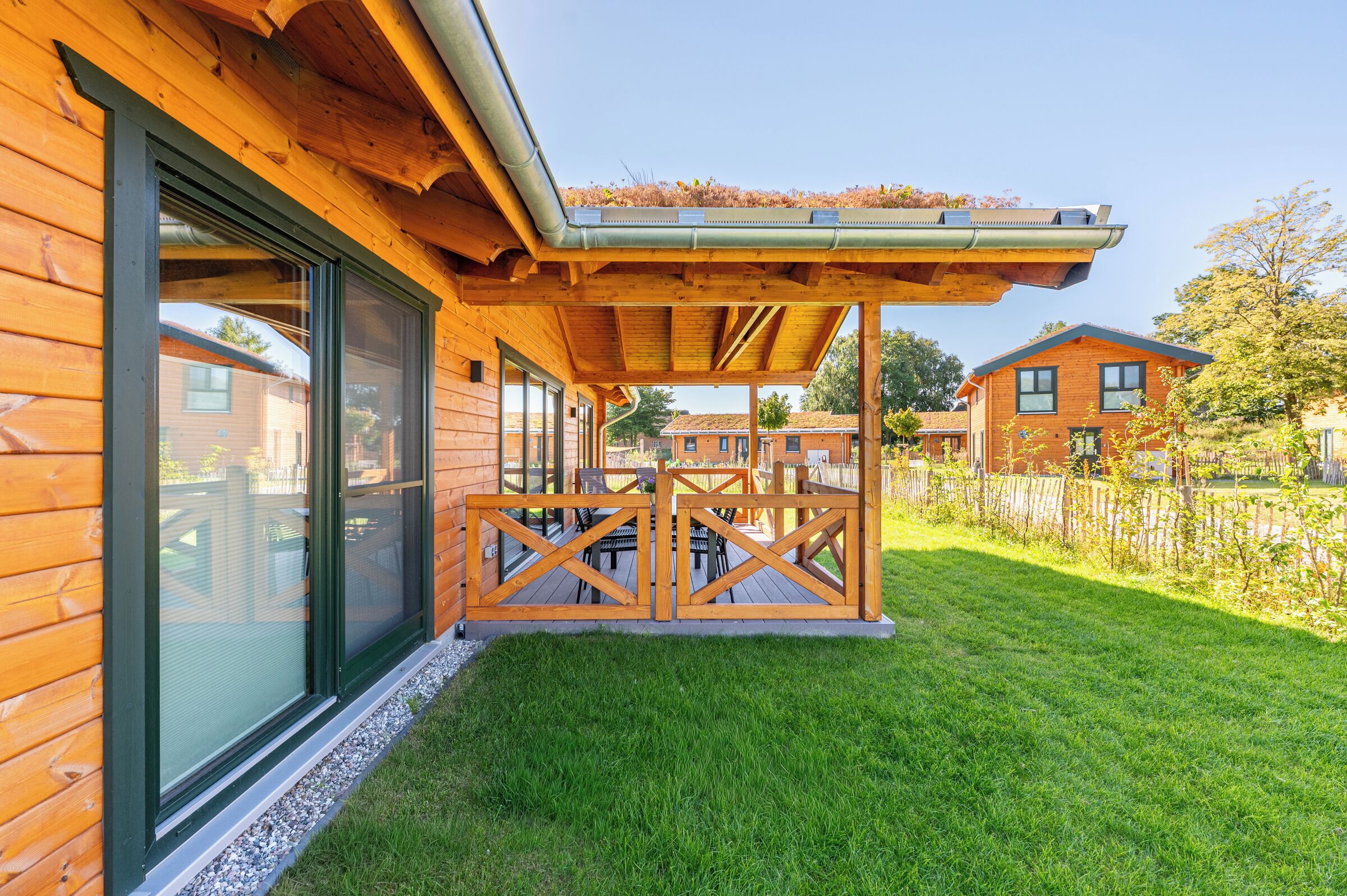 A wooden cabin with a covered patio area, a grassy yard, and a neighboring building.