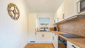 A modern kitchen with white cabinetry, a wooden countertop, and a wall-mounted clock. - Vacation home "Huus Plüschmors" in Kating for up to 4 people (Kating)
