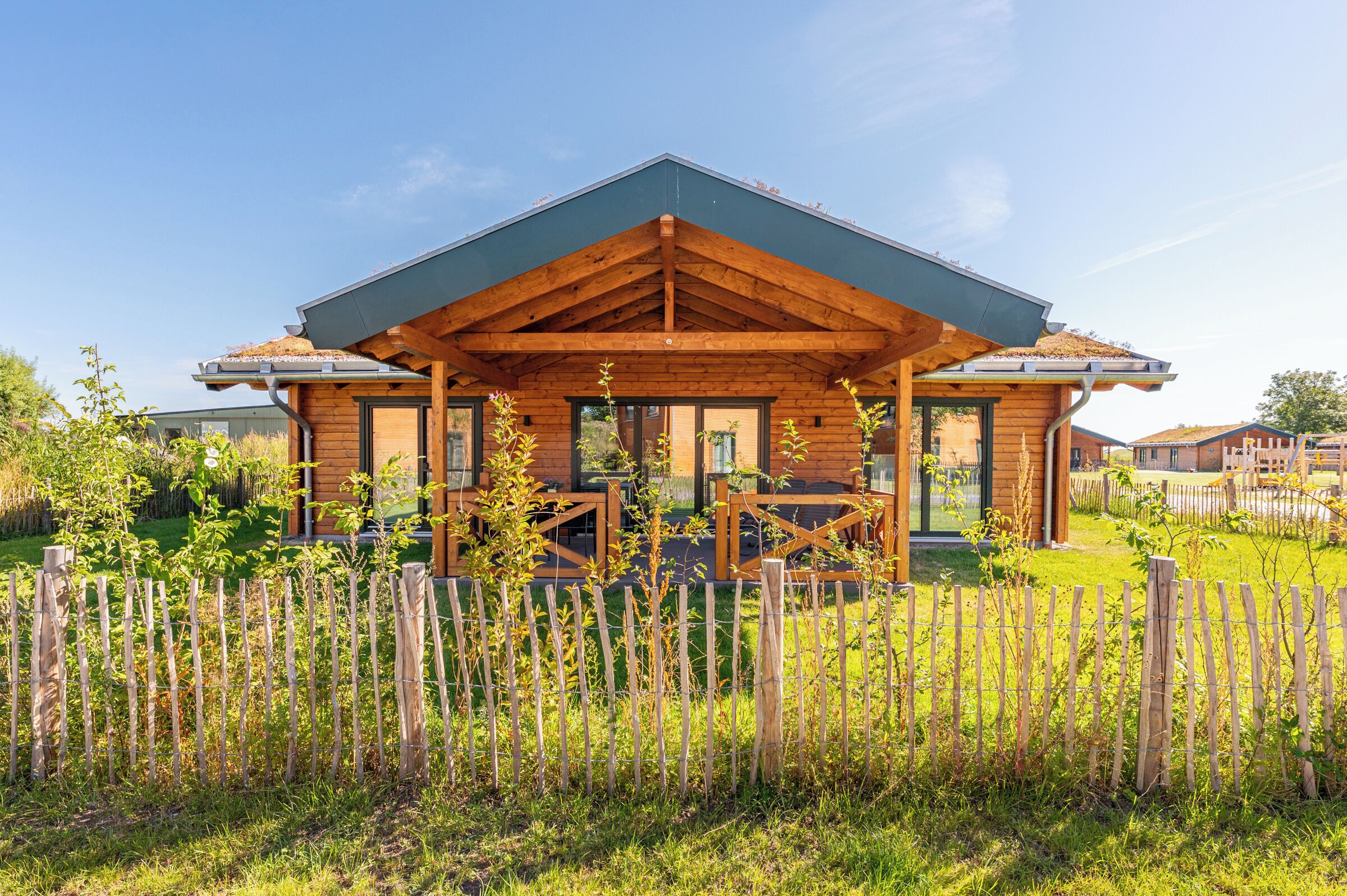 A wooden cabin with a covered porch, large windows, and a fenced garden.