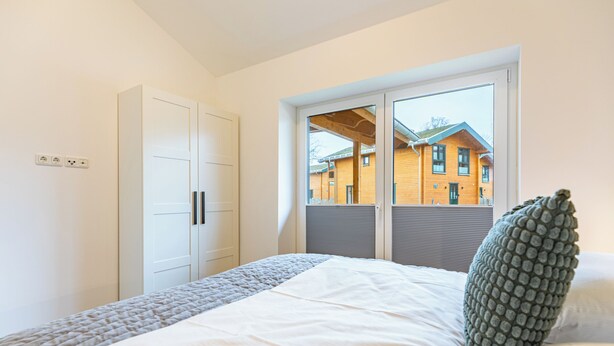 A bedroom with a bed, a wardrobe, a window with a view of a building, and a power outlet on the wall. - Vacation home "Huus Plüschmors" in Kating for up to 4 people (Kating)