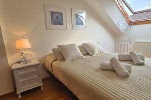 Een slaapkamer met een bed, kussens, een nachtkastje, een lamp en een raam met uitzicht.