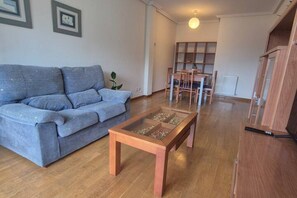 A living room with a sofa, a glass-top coffee table, and a dining area with chairs and a table.