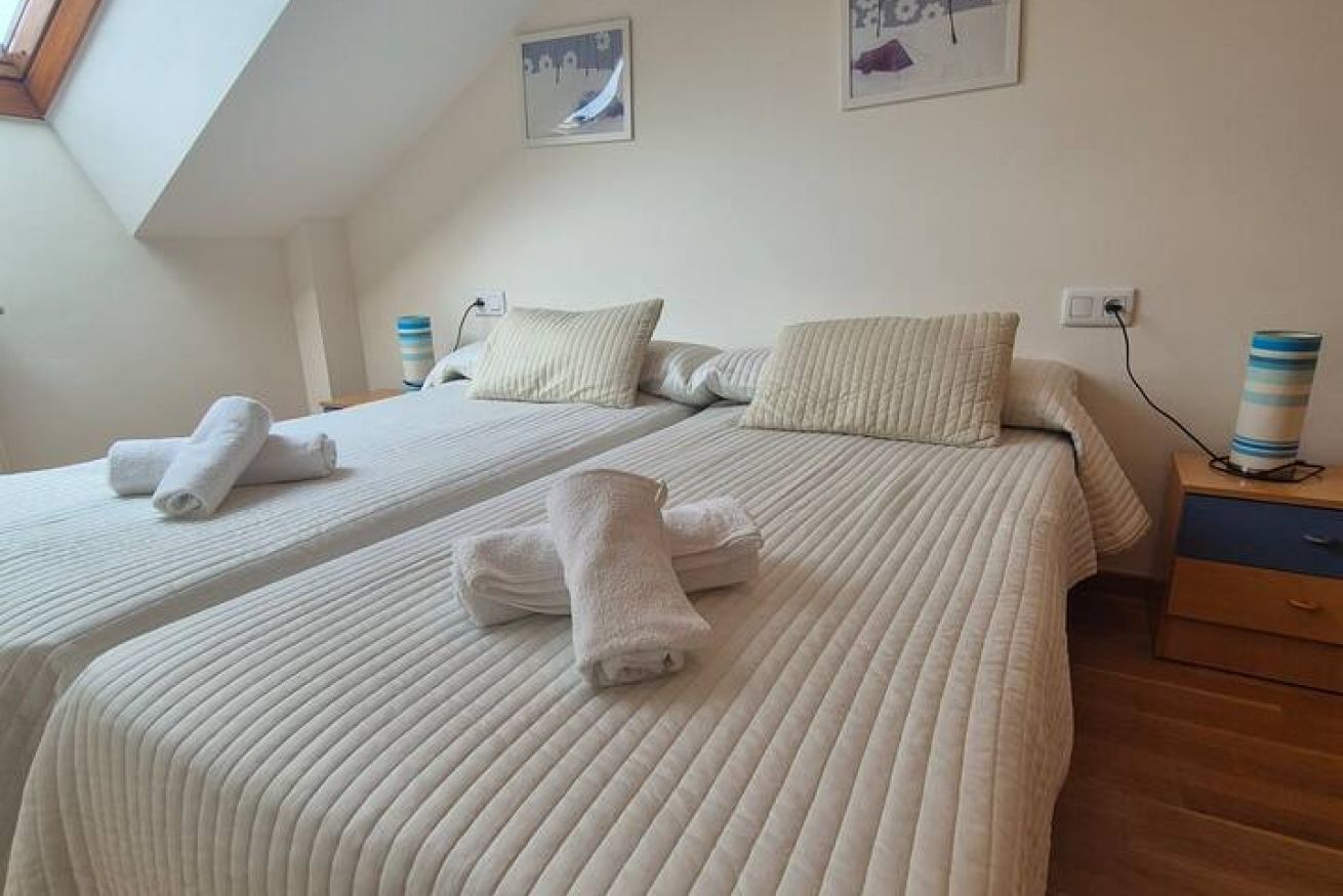 Een hotelkamer met twee bedden, elk met een gestreept dekbed en kussens, een nachtkastje met een lamp, en een raam met uitzicht.