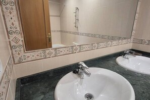 Un baño con dos lavamanos, una ducha y un espejo con azulejos decorativos.