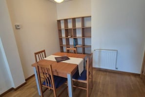 A small dining area with a table and chairs, a bookshelf, and a radiator.