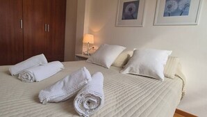 Un lit bien fait, avec des serviettes pliées, une lampe de chevet et des tableaux encadrés accrochés au mur.