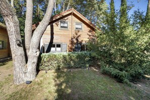 A wooden cabin with a gabled roof, surrounded by trees and a well-maintained lawn.