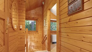 Interior de madera con una escalera de madera, una ventana con vistas a la vegetación y un cuadro en la pared.