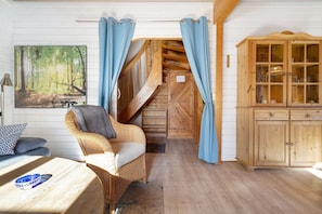 A room with a wooden staircase, a wicker chair, a cabinet, and a painting of a forest. - Holiday Home 'Wildgans' with Shared Terrace, Communal Garden and Wi-Fi (Lychen)