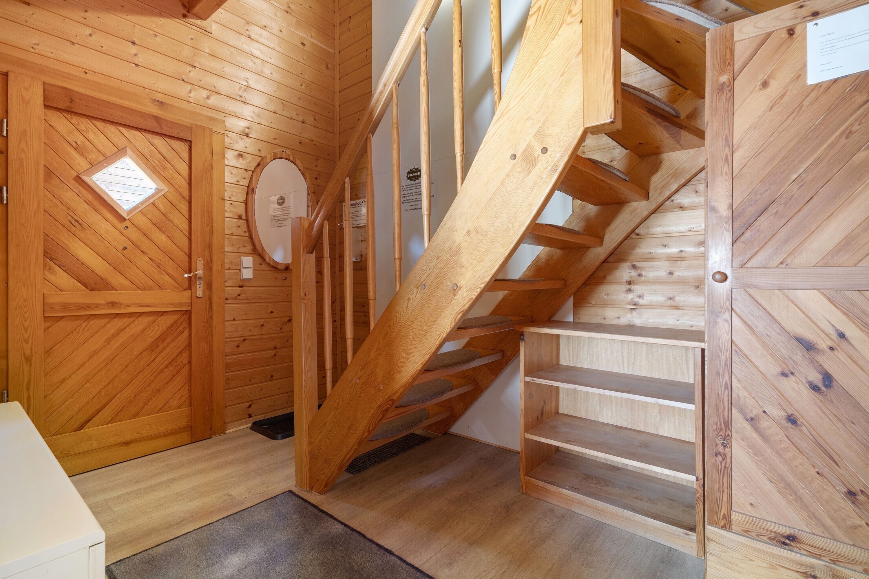 A wooden staircase leading to upper floors, a door with a window, and a small circular window on the wall.