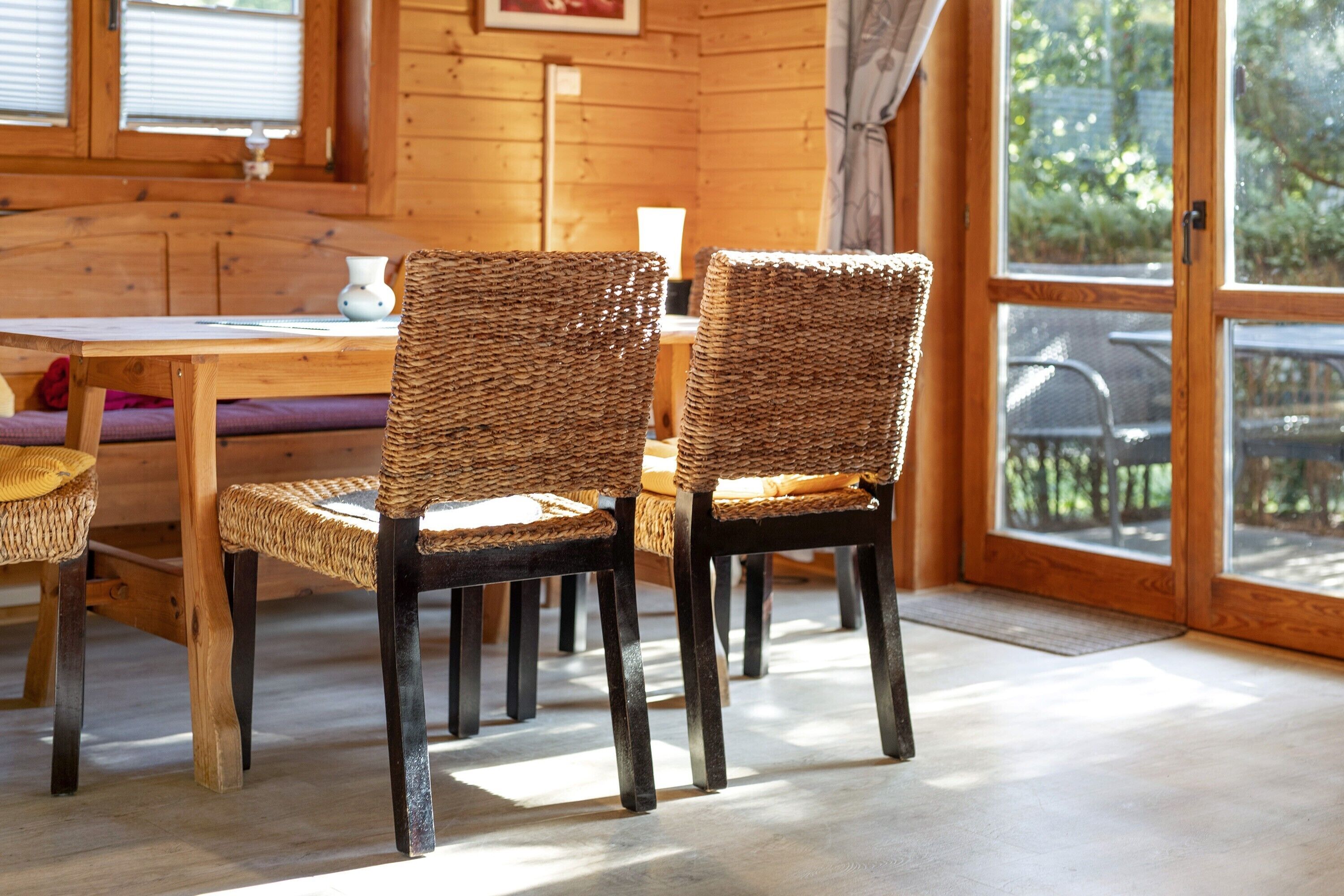 A wooden interior with wicker chairs, a wooden table, and a view through a glass door.