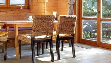 A wooden interior with wicker chairs, a wooden table, and a view through a glass door.