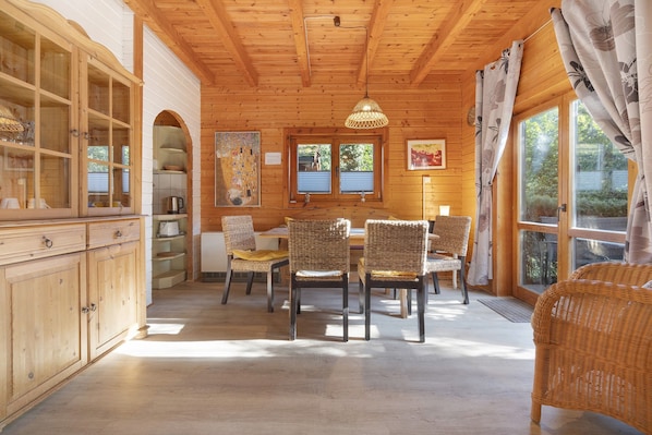 A wooden interior with a dining area, wicker chairs, a table, and a cabinet. - Holiday Home 'Wildgans' with Shared Terrace, Communal Garden and Wi-Fi (Lychen)