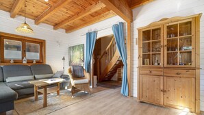 Un salón con suelo de madera, un sofá, una silla de mimbre, un mueble de madera con puertas de cristal y una escalera.