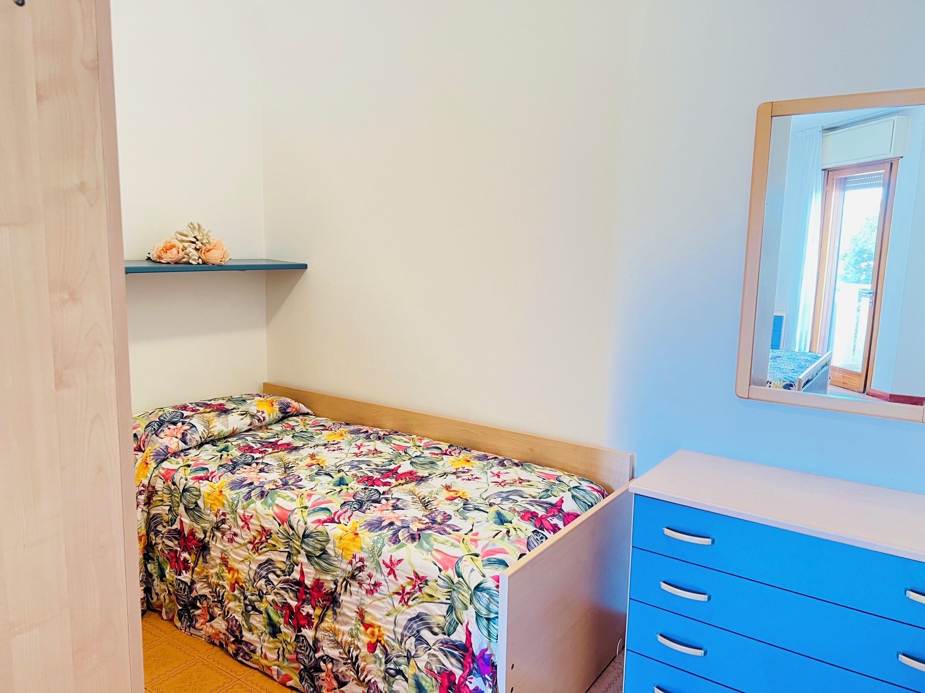 Une chambre à coucher comprenant un lit, une commode, un miroir et une étagère ornée d’objets décoratifs.