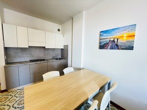 A modern kitchen with grey cabinets, a wooden dining table, and a painting of a sunset on the wall. - Sea View Apartment - Beahost (San Michele al Tagliamento)