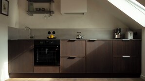 A modern kitchen with dark wooden cabinets, a built-in oven, a kettle, and a coffee maker. - Carefully renovated apartment with sea view in Saint Cado (Belz)